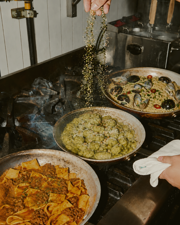 Three pans of food on a stovetop with someone seasoning one of them.