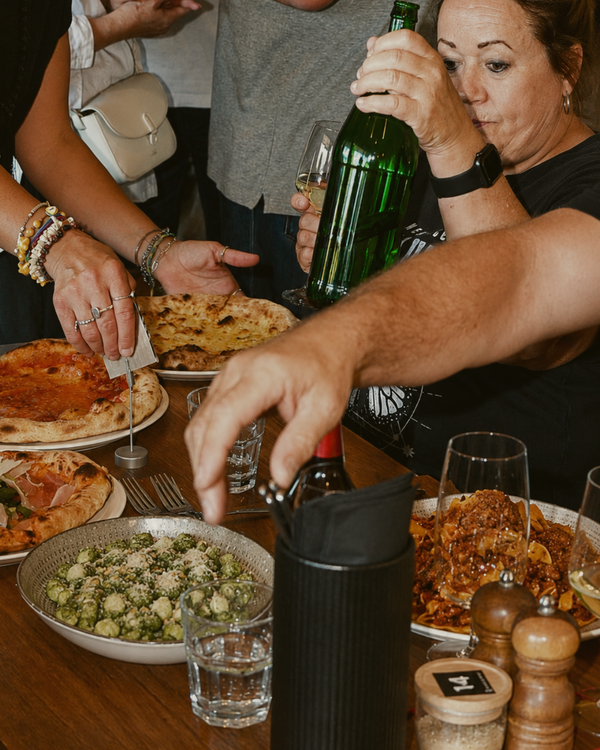 Person opening a bottle of wine at a table with food and drinks.