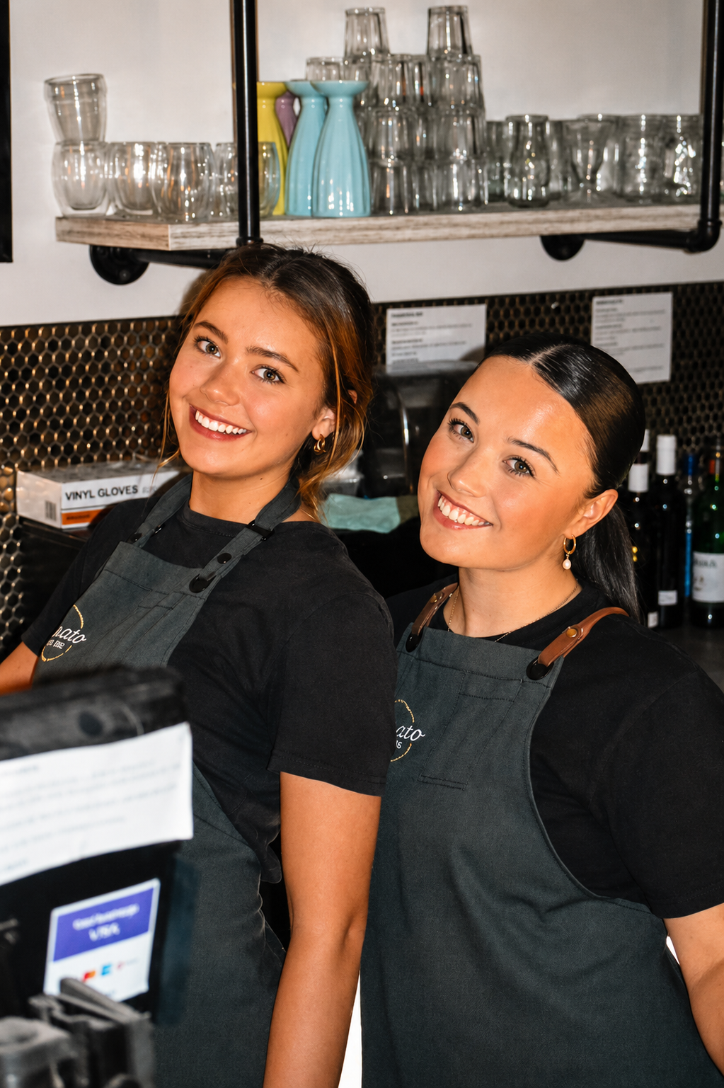 Two women in aprons standing behind a counter in a coffee shop.