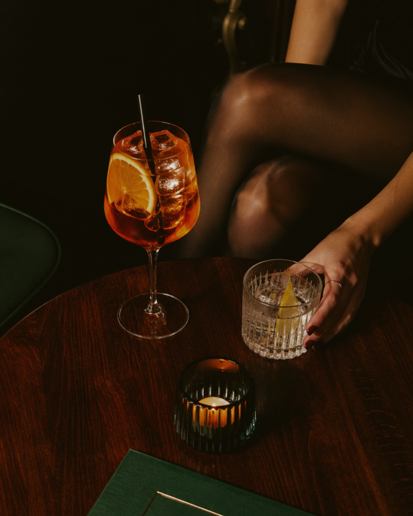 Two cocktails on a wooden table with a person's hand reaching for one of them.
